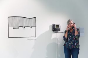 White wall with black and white graphic and woman talking on a wall-mounted phone.